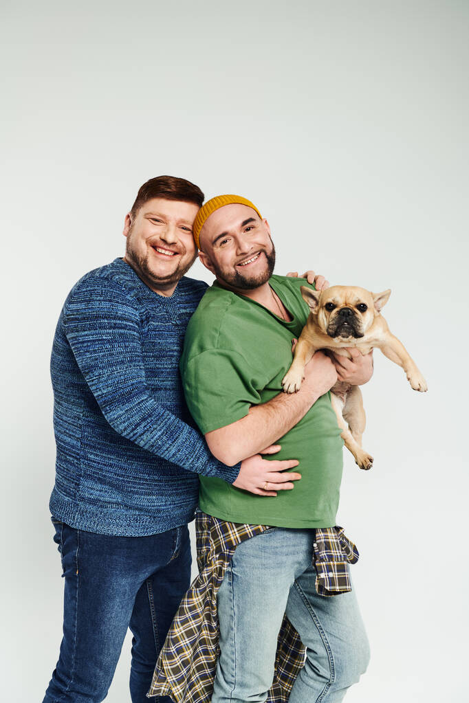Zwei Männer umarmen sich, während sie eine süße französische Bulldogge in der Hand halten. - Foto, Bild