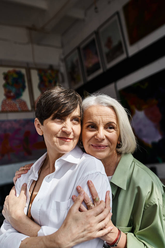 Two mature women hugging in an art studio. - Photo, Image