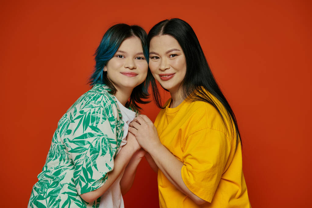 Uma mãe asiática e sua filha adolescente estão lado a lado na frente de uma impressionante parede vermelha. - Foto, Imagem