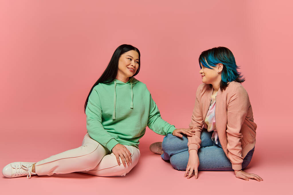Zwei Frauen, eine asiatische Mutter und ihre Tochter im Teenageralter, sitzen auf dem Boden und unterhalten sich und stellen Nähe und Verbundenheit dar. - Foto, Bild