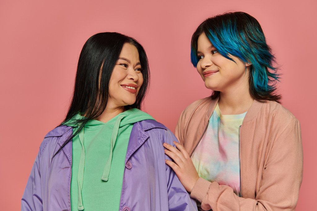Asian mother and teenage daughter standing together in casual wear in front of a vibrant pink background. - Photo, Image
