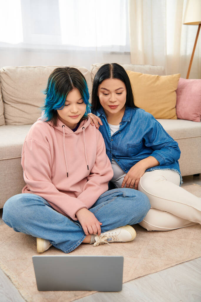 An Asian mother and her teenage daughter, in casual attire, sit on the floor together, engrossed in using a laptop. - Photo, Image