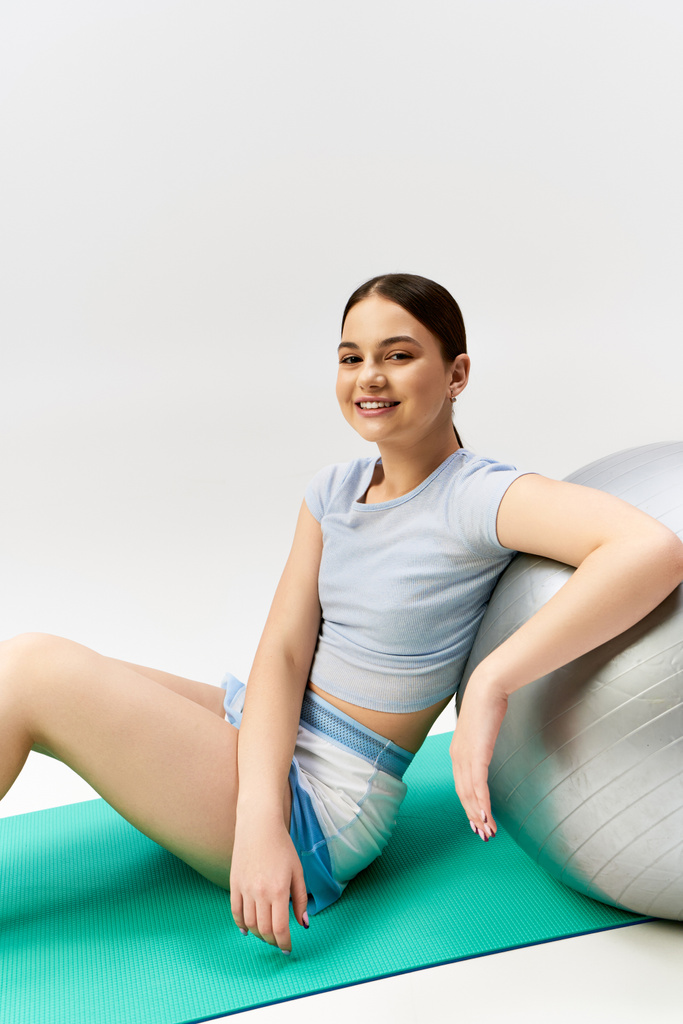 Ładna, brunetka nastolatka w sportowym stroju z wdziękiem balansuje na piłce do jogi w studio - Zdjęcie, obraz