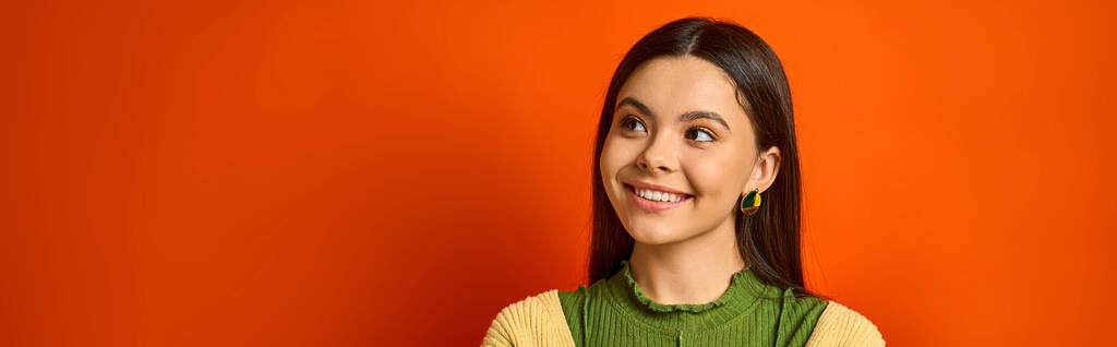 Yeşil tişörtlü güzel, esmer bir genç kız turuncu stüdyo arka planında neşeyle gülümsüyor.. - Fotoğraf, Görsel