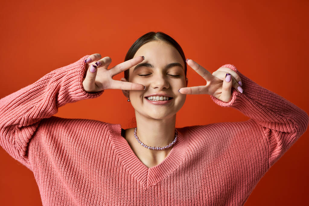 Een brunette tienermeisje in casual kleding glimlacht terwijl het maken van een vrede teken met haar handen, symboliseren eenheid en harmonie. - Foto, afbeelding
