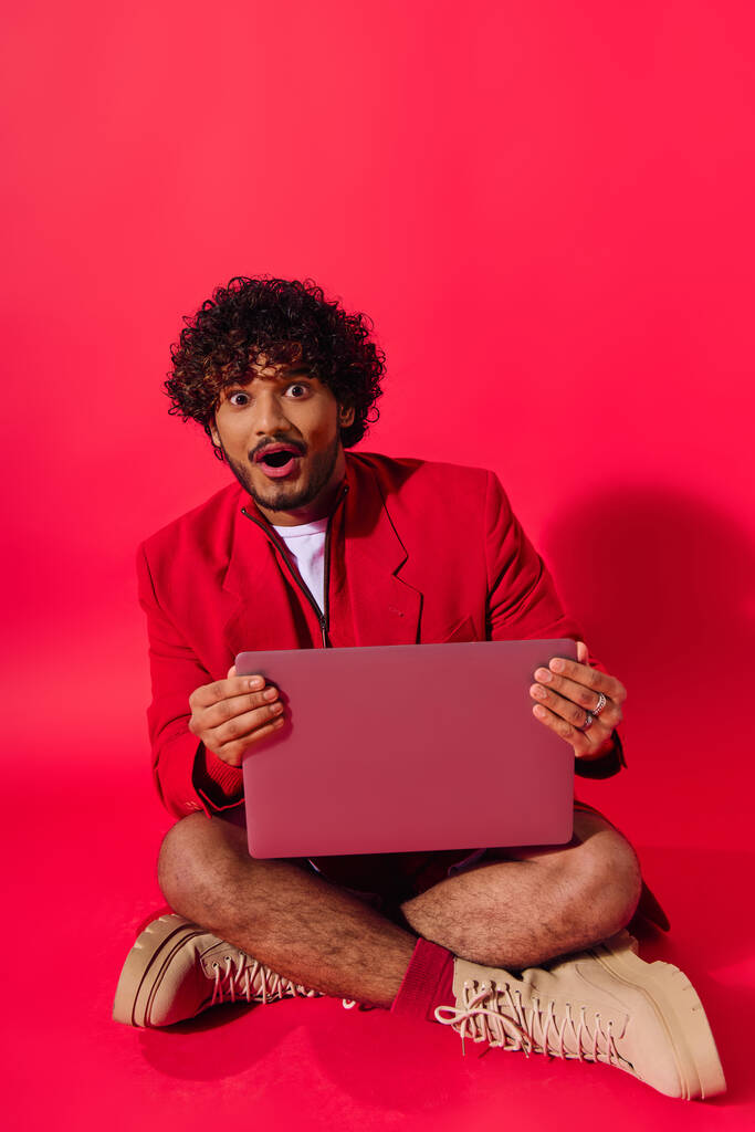 Un homme en tenue vibrante est assis sur le sol, absorbé dans son ordinateur portable. - Photo, image