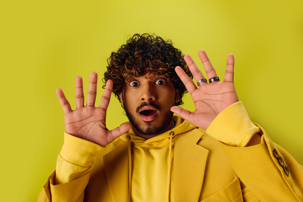 Hombre indio guapo en chaqueta amarilla vibrante que se divierte posando con las manos en la cara. - Foto, imagen