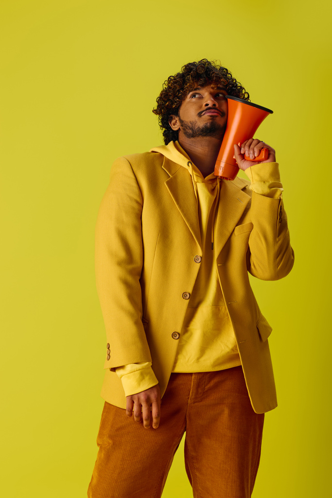 Knappe Indiase man in geel jasje met rode megafoon tegen een levendige achtergrond. - Foto, afbeelding