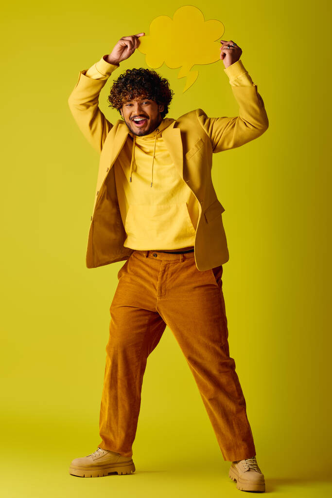 Przystojny Indianin w żółtej koszuli i brązowych spodniach, pozujący przed żywym tłem. - Zdjęcie, obraz