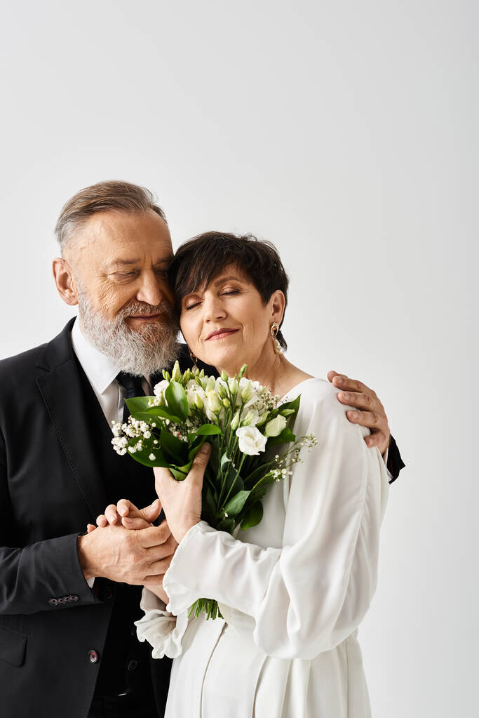 Een bruid en bruidegom van middelbare leeftijd in trouwjurken vieren hun speciale dag in een studio door naast elkaar te staan. - Foto, afbeelding