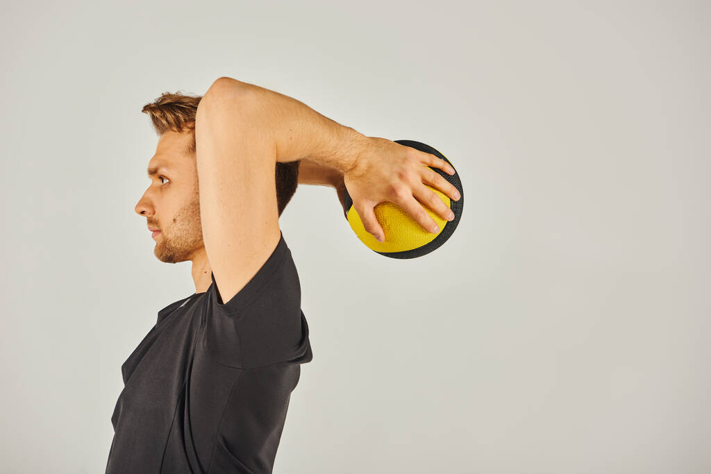 Jovem desportista em uso ativo vigorosamente exercícios com uma bola amarela em um estúdio com um fundo cinza. - Foto, Imagem