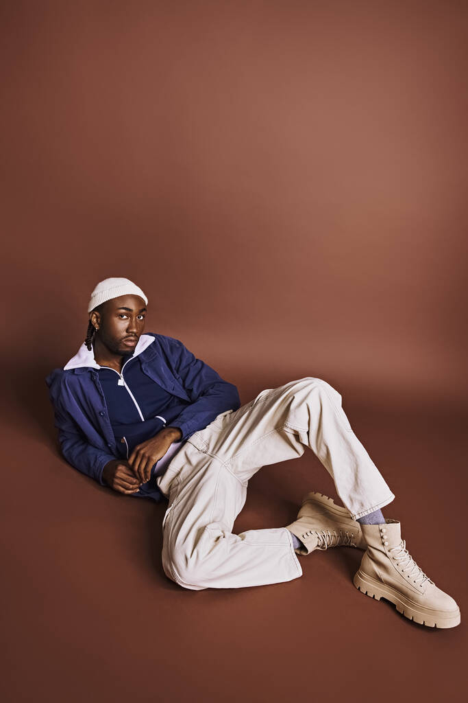 Egy fiatal afro-amerikai férfi ül a földön, elegáns kalapban.. - Fotó, kép