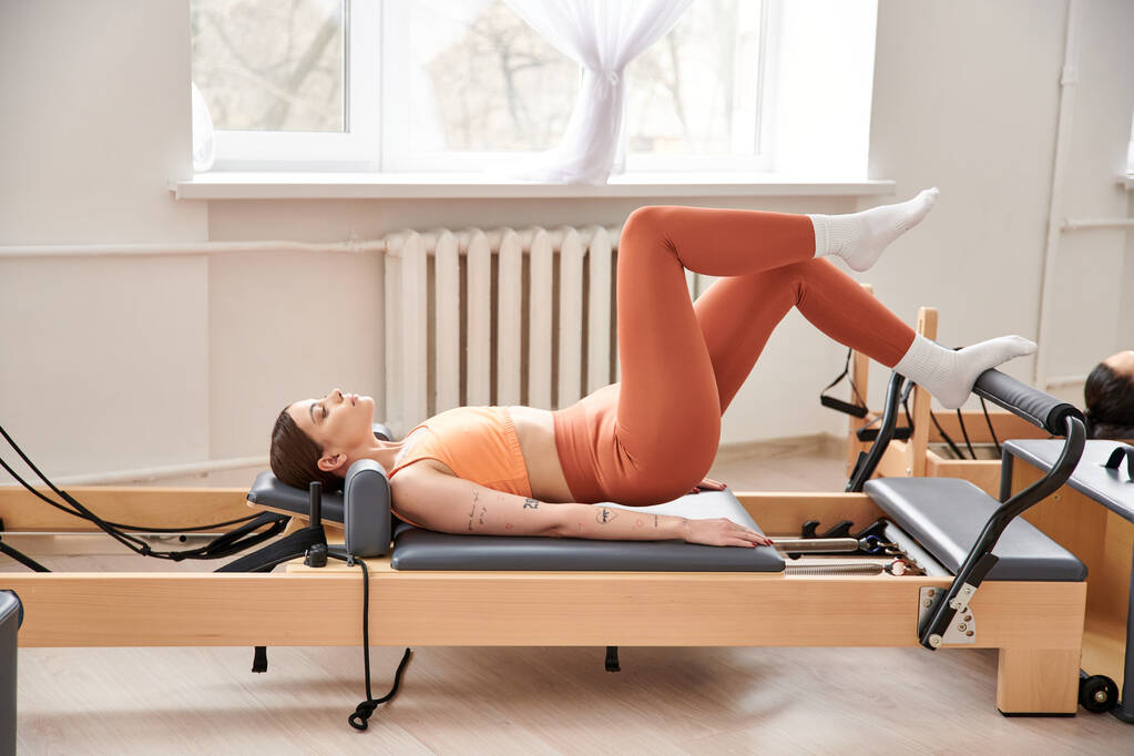 Eine sportliche Frau in orangefarbenem Oberteil übt sich in Pilates. - Foto, Bild