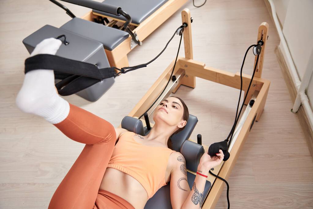 Een sportieve vrouw liggend op een stationaire trainingsmachine tijdens een pilates les. - Foto, afbeelding