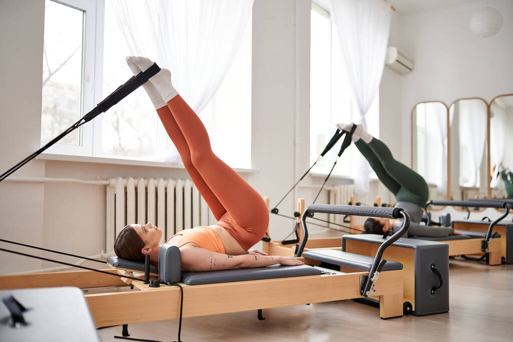 A sporty woman in an orange top stretches her back during a Pilates lesson. - Photo, Image