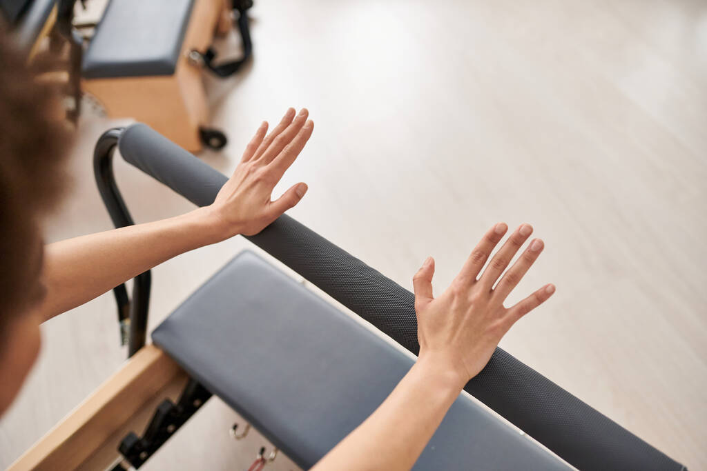 A pretty, sporty woman stretches her arms on equipment during a Pilates lesson. - Photo, Image