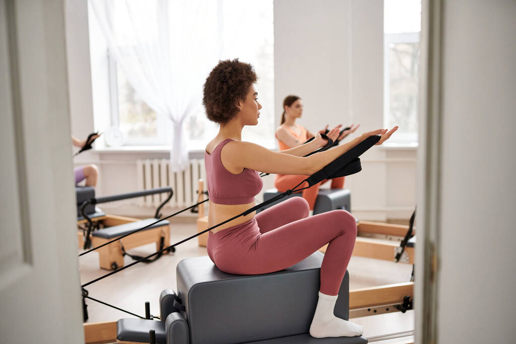 Gut aussehende Frauen in kuscheliger Kleidung üben gemeinsam Pilates in einem Fitnessstudio. - Foto, Bild