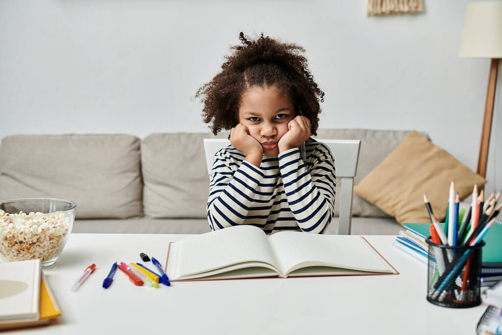 Una niña absorta en un libro en una mesa, aburrida - Foto, imagen