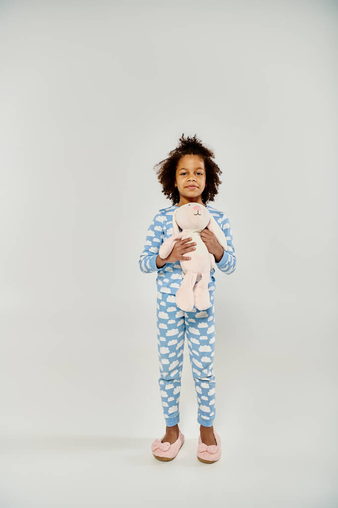 Egy boldog afro-amerikai lány pizsamában gyengéden tart egy plüssmacit, kifejezve a kényelem és biztonság érzését.. - Fotó, kép