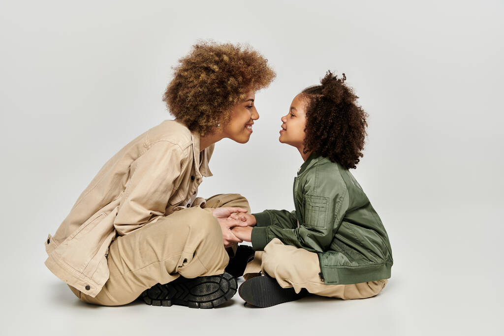 Kędzierzawa Afroamerykanka matka i córka w stylowych ciuchach siedzą na podłodze, dzieląc delikatną chwilę razem. - Zdjęcie, obraz