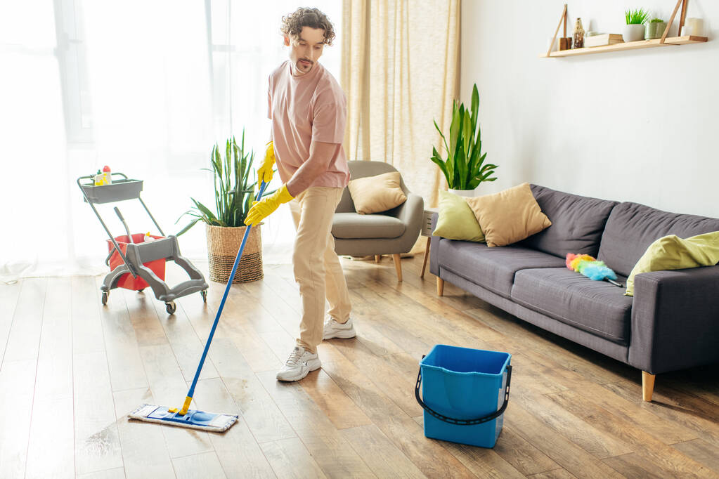 Handsome man in cozy homewear gracefully mopping the floor. - Photo, Image