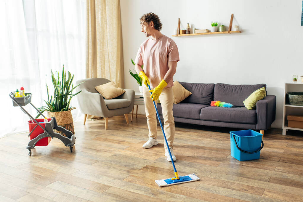 Mies kodikas kotivaatteet energisesti moppaa olohuoneen lattiaa. - Valokuva, kuva