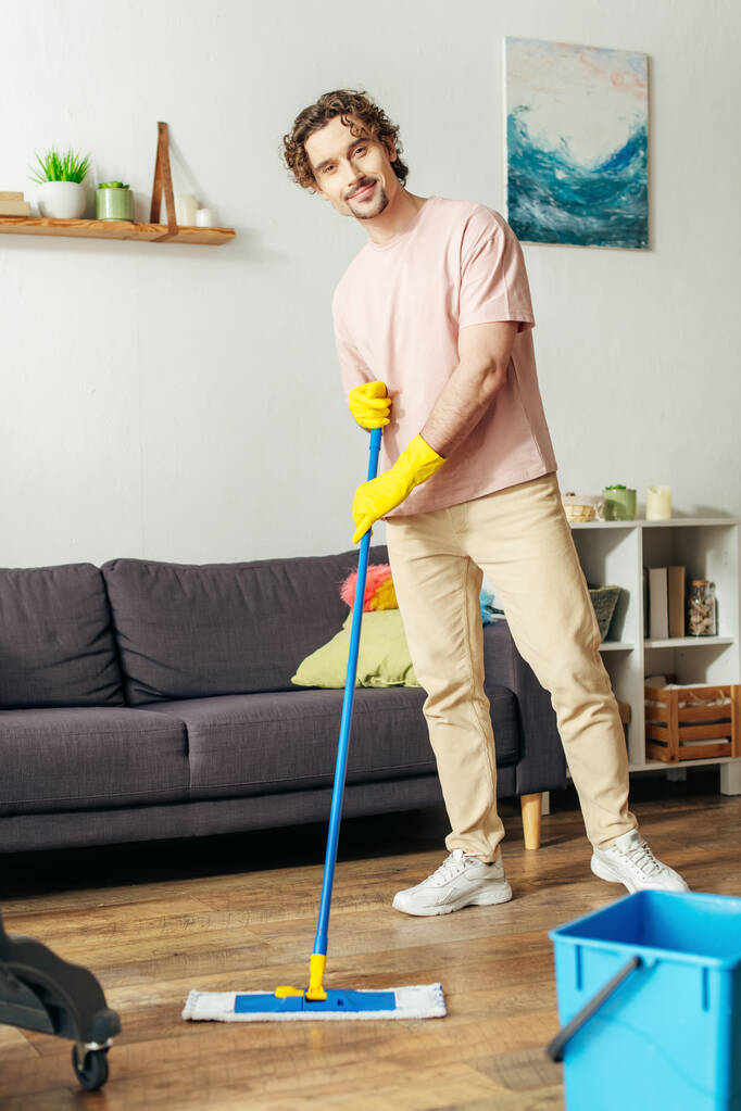 Hezký muž v útulných domácích šatech utírá podlahu. - Fotografie, Obrázek