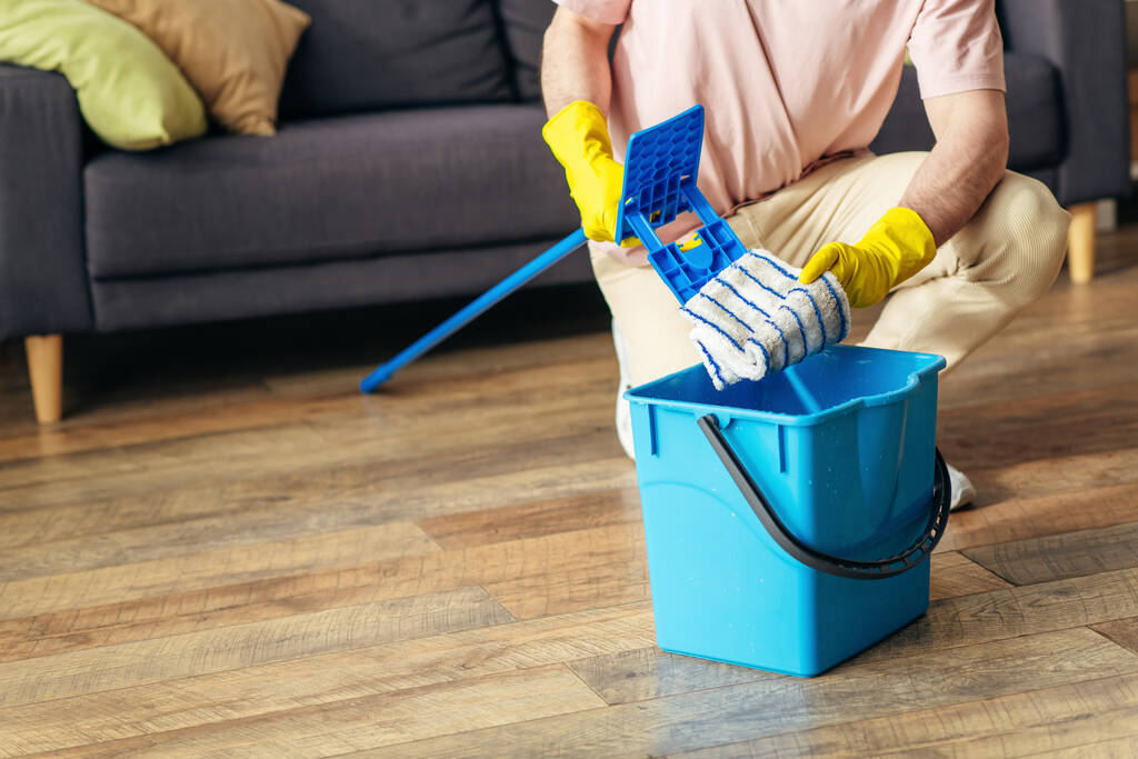 Hezký muž v útulném oblečení pečlivě utírá podlahu obývacího pokoje. - Fotografie, Obrázek