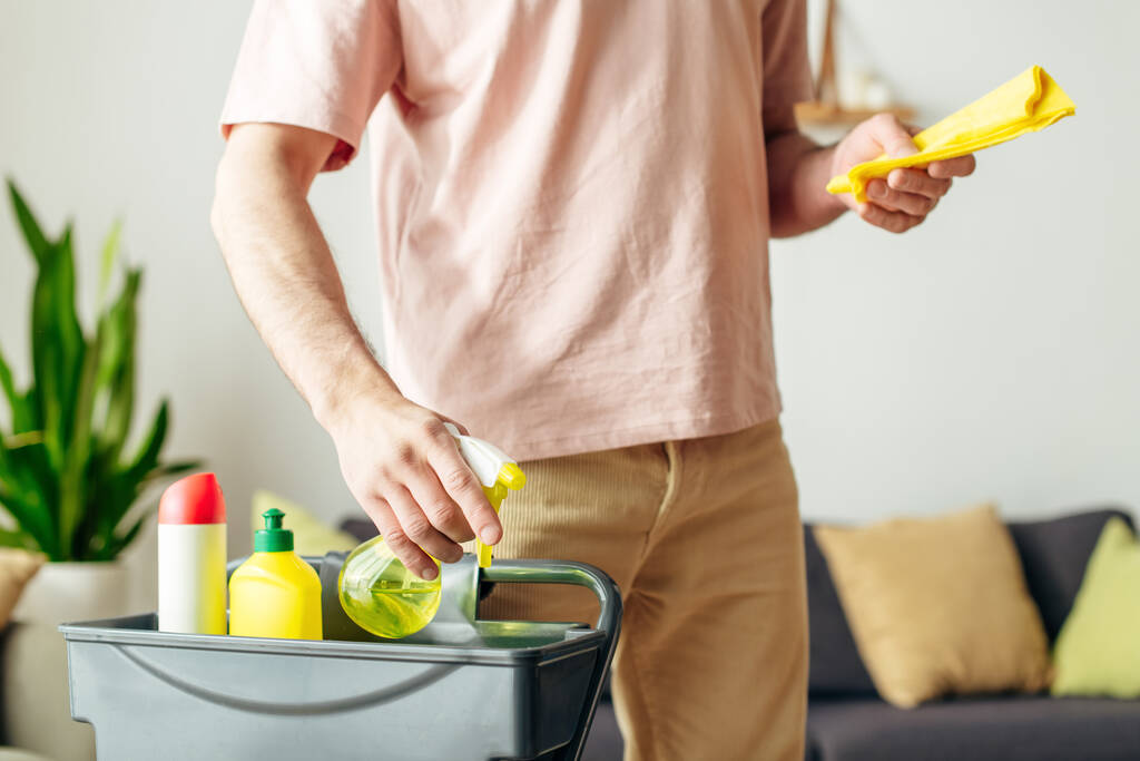 Un homme en tenue confortable nettoie un salon avec des sprays jaunes. - Photo, image