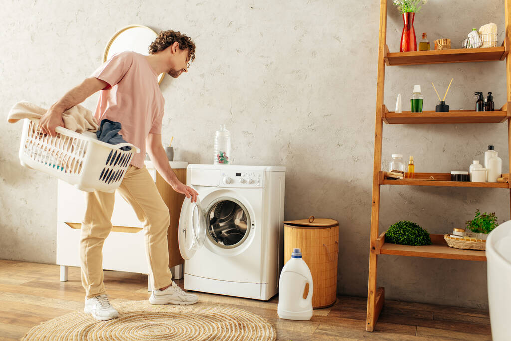 Çamaşır sepetini çamaşır makinesiyle tutan rahat ev elbiseli yakışıklı bir adam.. - Fotoğraf, Görsel