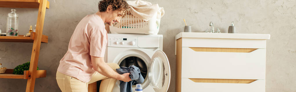 Ein Mann lädt vorsichtig Kleidung in eine Waschmaschine. - Foto, Bild