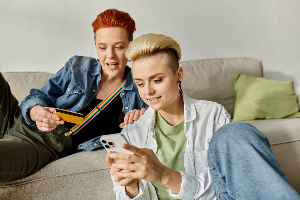 Dwie krótkowłose kobiety siedzą na kanapie, pochłonięte ekranem telefonu komórkowego, dzieląc chwilę intymności i połączenia. - Zdjęcie, obraz