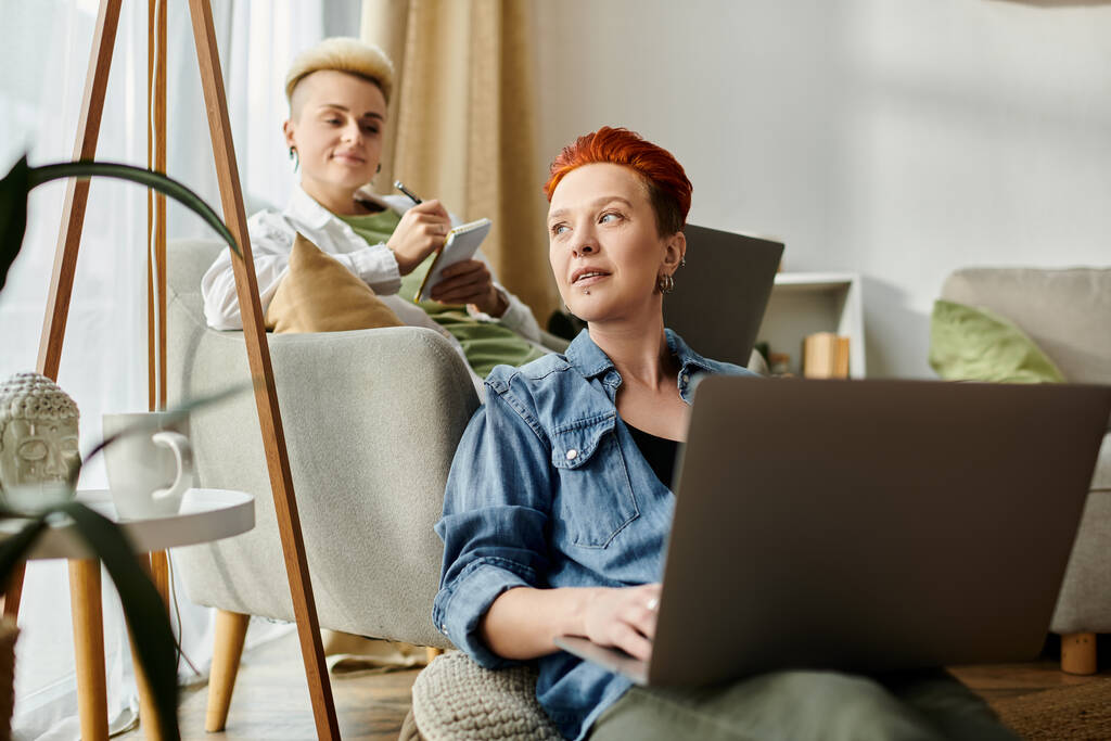 Lesbijska para z krótkimi włosami siedzi na kanapie, każda pochłonięta ekranami laptopa. - Zdjęcie, obraz