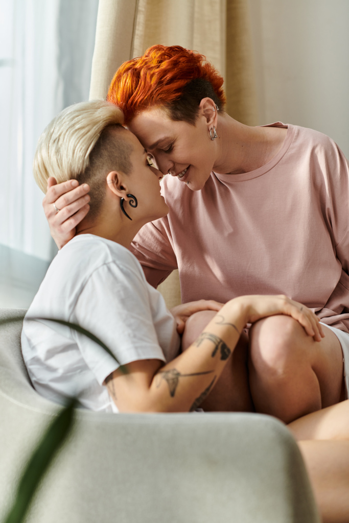 Dwie kobiety z krótkimi włosami przytulają się czule na kanapie w ciepłym i kameralnym otoczeniu, promieniując miłością i ciepłem. - Zdjęcie, obraz