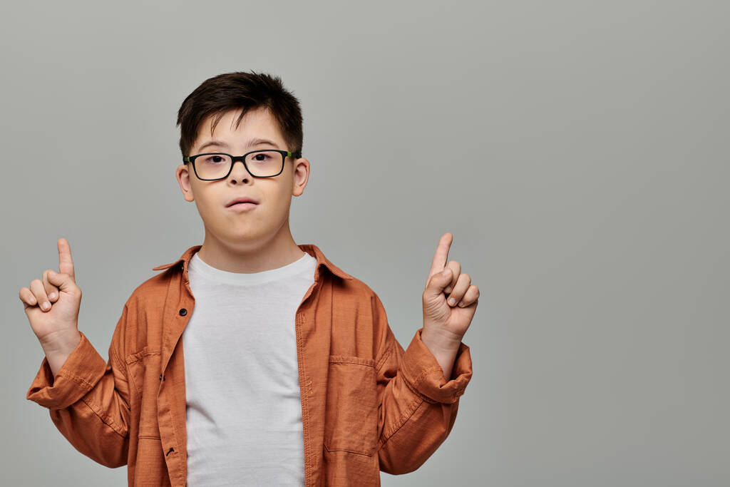 Un niño pequeño con síndrome de Down con gafas gestos juguetones con el dedo. - Foto, Imagen