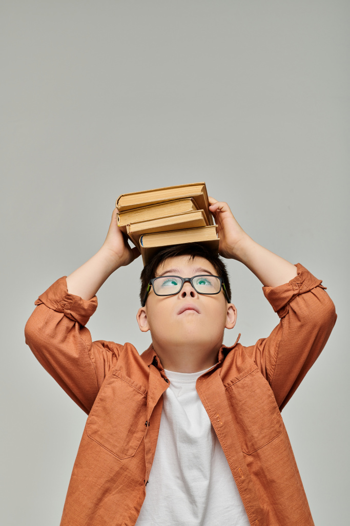 Um menino com síndrome de Down equilibra uma pilha de livros na cabeça. - Foto, Imagem