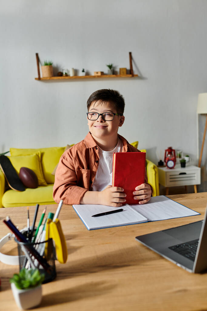Ein Junge mit Down-Syndrom sitzt am Schreibtisch und benutzt Laptop und Notizbuch. - Foto, Bild