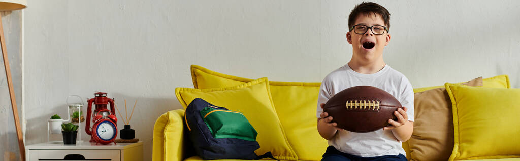 Malý chlapec šťastně drží míč, zatímco sedí na gauči doma. - Fotografie, Obrázek