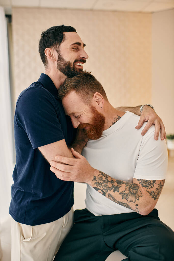 Dos hombres en una acogedora habitación compartiendo un cálido abrazo, expresando amor y conexión en un momento de alegría. - Foto, Imagen