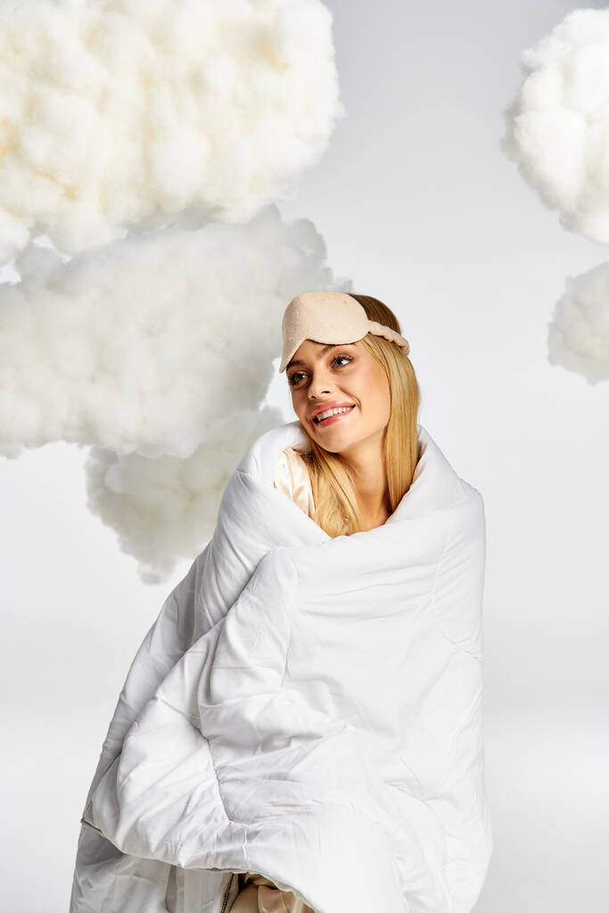 Una donna bionda sognante in pigiama accogliente sorride mentre avvolto in una coperta. - Foto, immagini