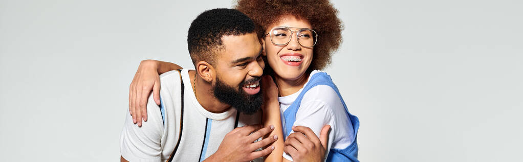 Twee stijlvol geklede Afro-Amerikaanse vrienden die elkaar omhelzen met warmte en genegenheid op een grijze achtergrond. - Foto, afbeelding