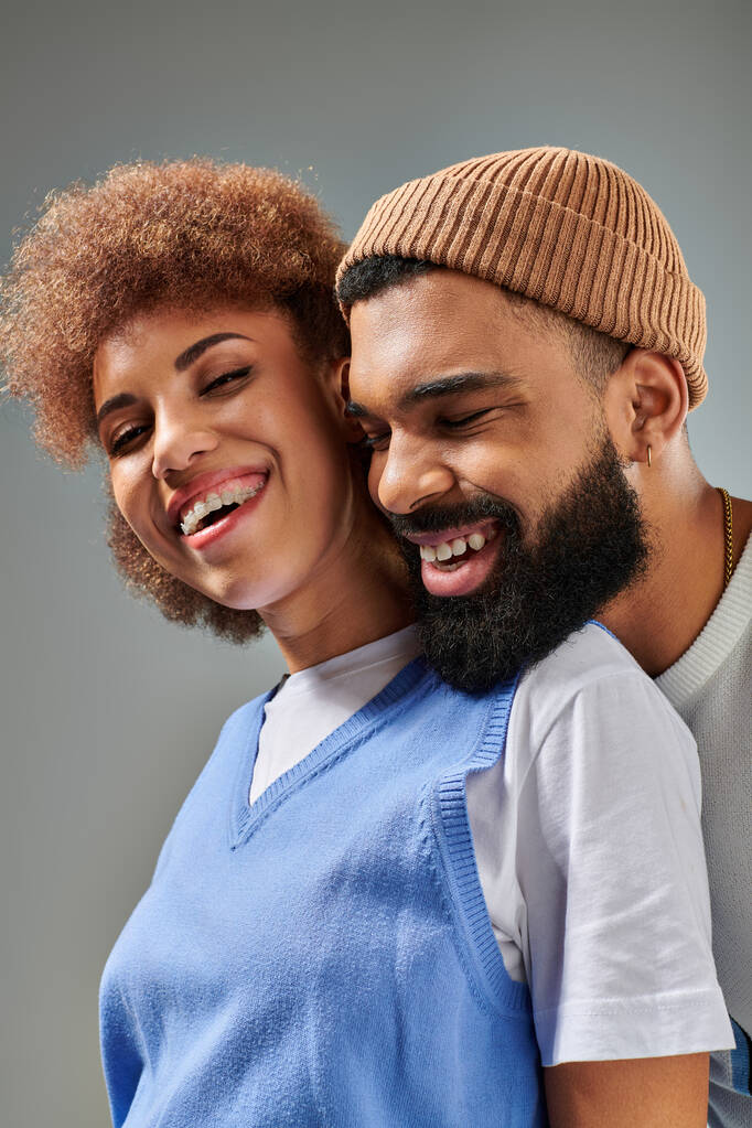 Un hombre y una mujer afroamericanos con ropa elegante riéndose juntos sobre un fondo gris. - Foto, imagen