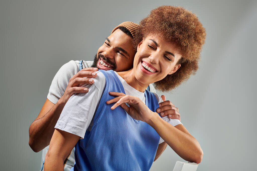 Amigos afroamericanos con ropa elegante abrazándose, mostrando amistad y conexión sobre un fondo gris. - Foto, Imagen