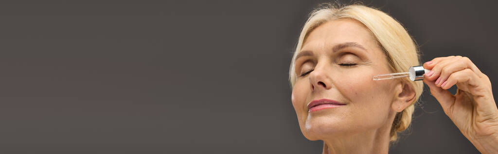 Heerlijk volwassen vrouw toepassen serum op een grijze achtergrond. - Foto, afbeelding