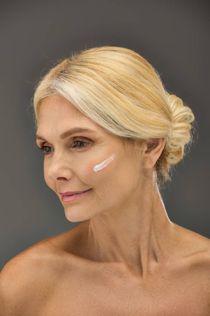 Mujer madura mostrando su rutina de cuidado de la piel con crema en la cara. - Foto, Imagen