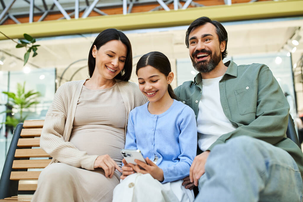 Радісна сім'я з чотирьох сидить разом на лавці в галасливому торговому центрі, посміхаючись і насолоджуючись своїм часом. - Фото, зображення