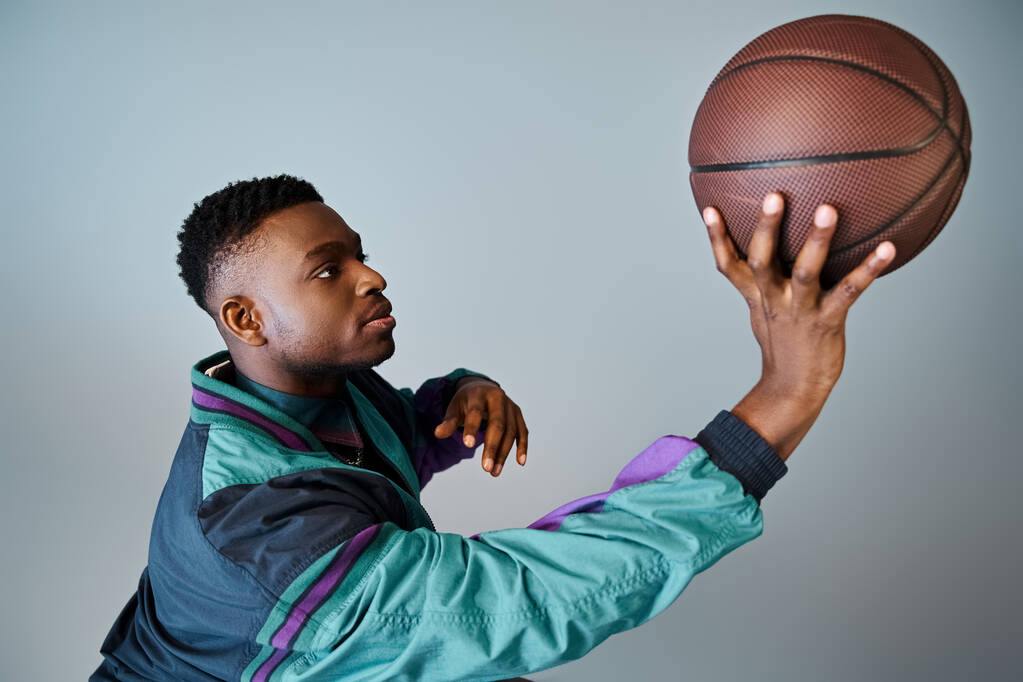 Ein modischer junger Afroamerikaner in stylischer Kleidung hält einen Basketball in der Hand. - Foto, Bild