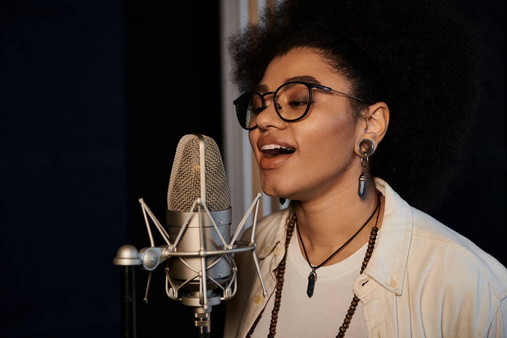 Kobieta w okularach śpiewa namiętnie do mikrofonu podczas próby zespołu muzycznego w studiu nagraniowym. - Zdjęcie, obraz