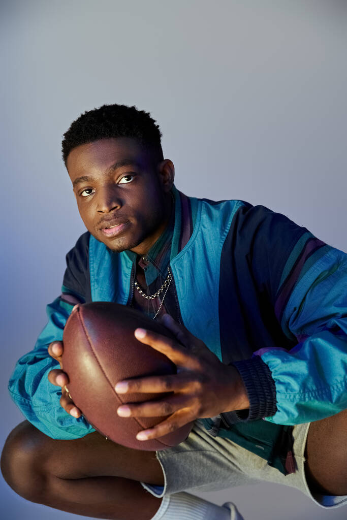 A stylish African American man crouching down while holding a football. - Photo, Image