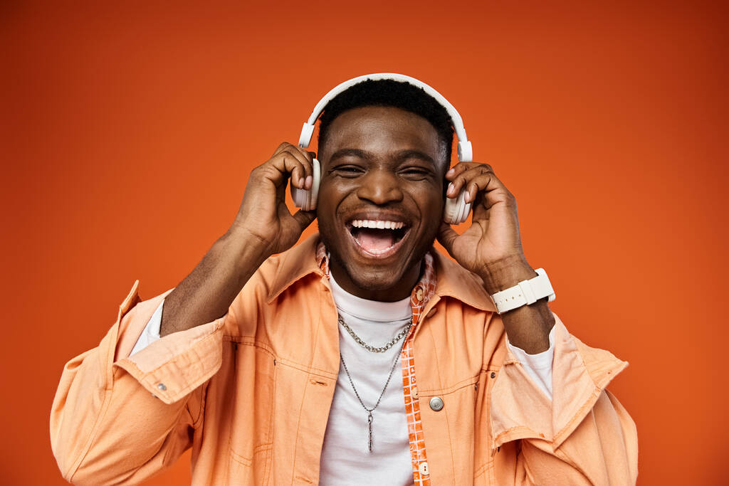 Stijlvolle zwarte man die naar muziek luistert met een koptelefoon op een fel oranje achtergrond. - Foto, afbeelding
